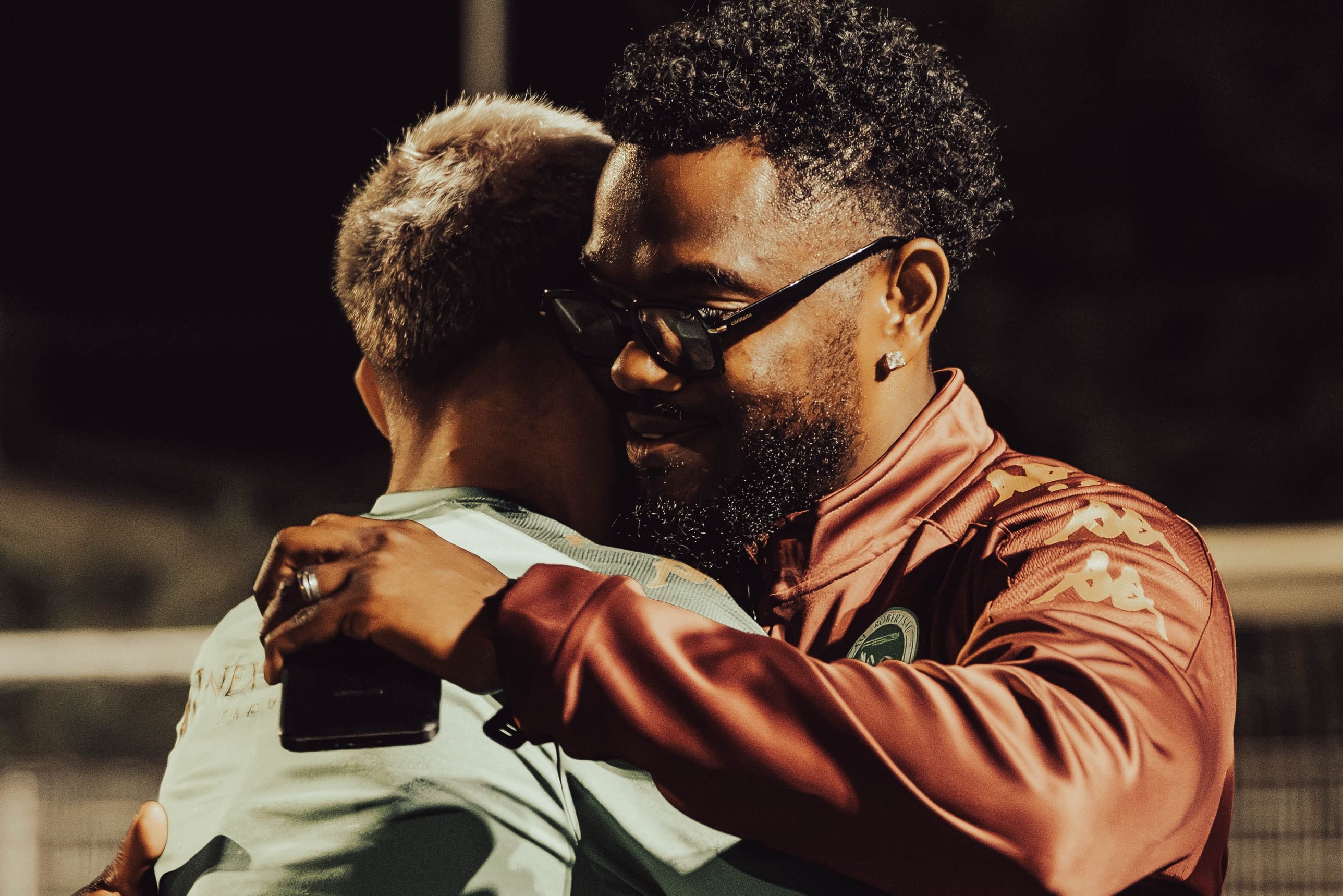 Accolade entre deux hommes au bord d’un terrain de football