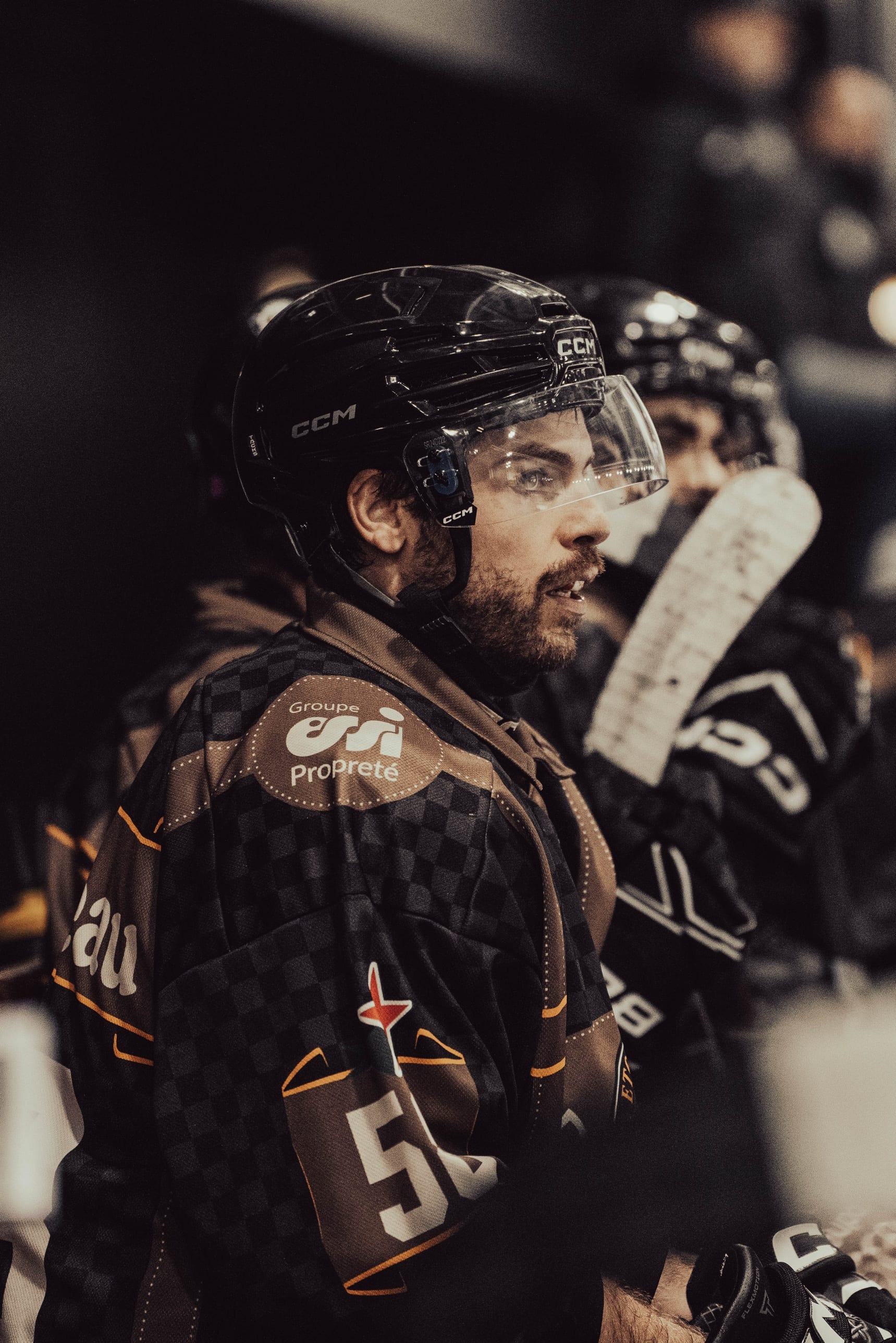 Joueur de hockey sur glace de profil, casque et visière, sur le banc